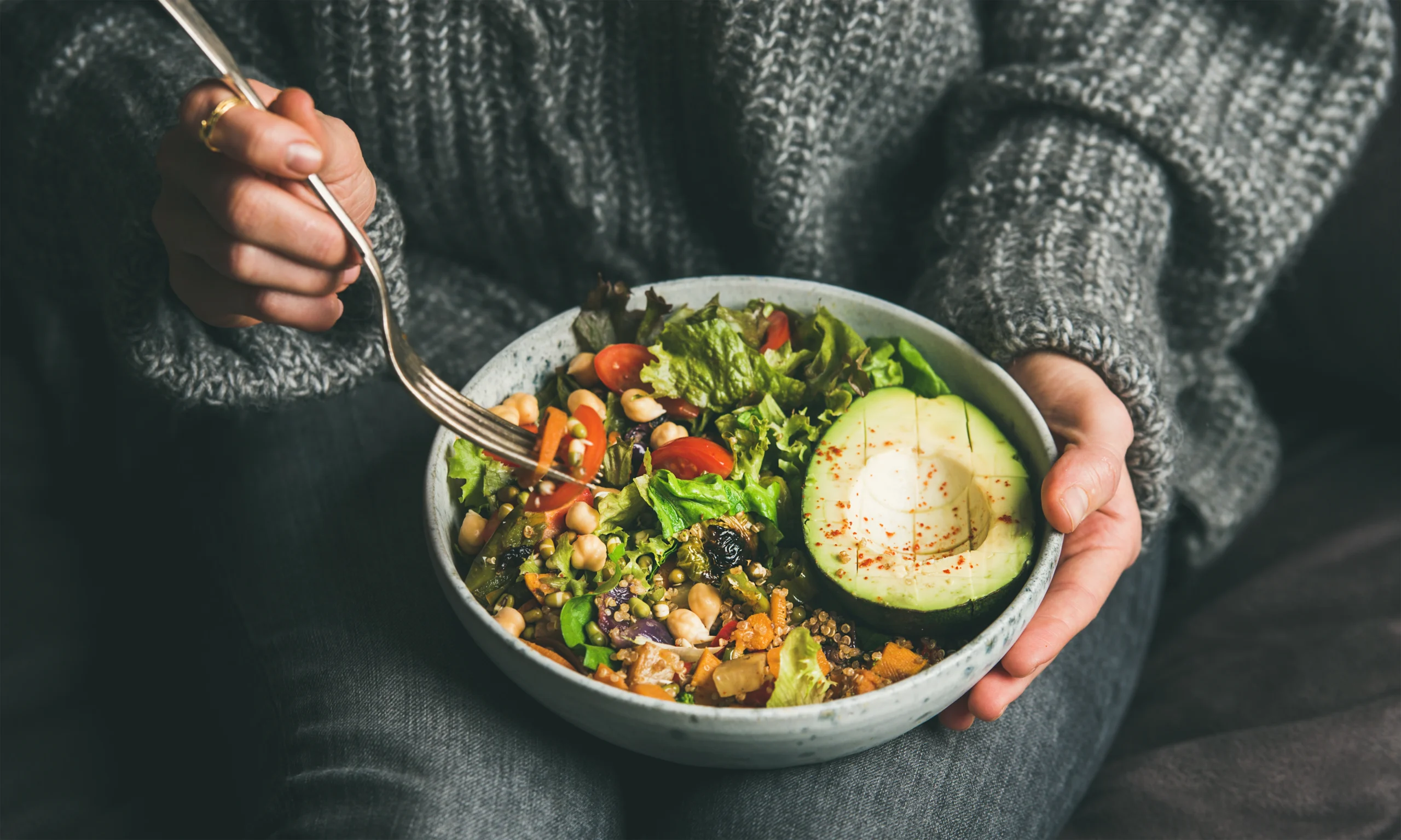 Person eating a healthy salad bowl with avocado, chickpeas, and fresh vegetables